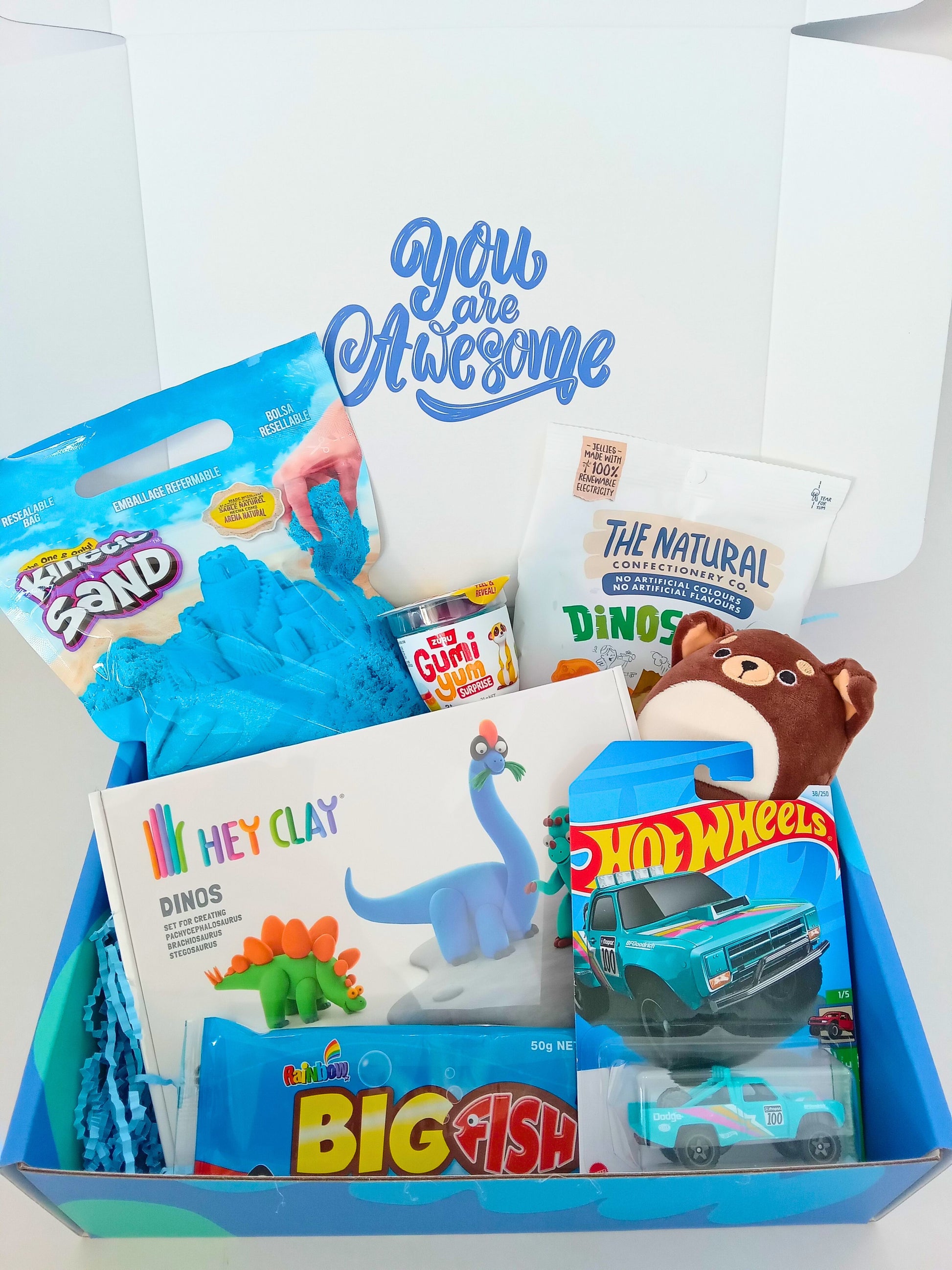 Gift basket with toys and activities for children, including a dinosaur hey clay, squishmallow and Hot Wheels car, plus treats.