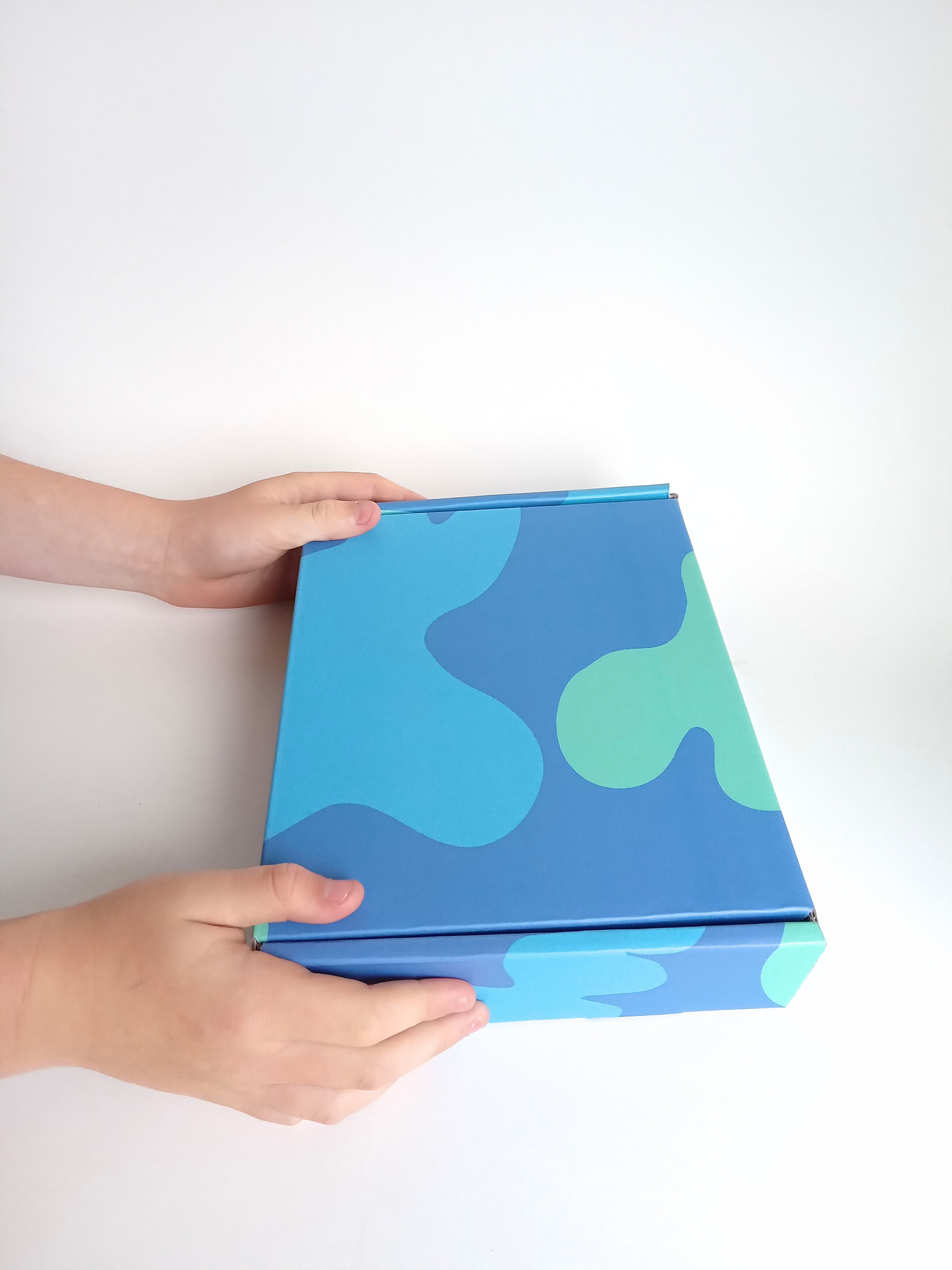 Kids gift box in bright blue blobs design, held by two hands
